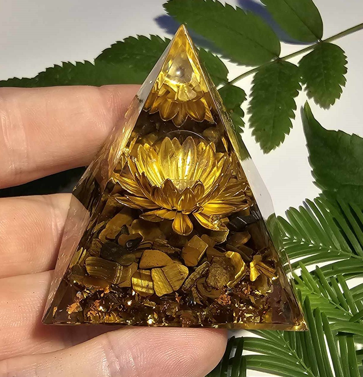 Håndlavet orgonit pyramide med gylden lotusblomst, tigerøje sten og kobberdetaljer, fra Naturens Skatte. Perfekt til beskyttelse og æstetisk energi.